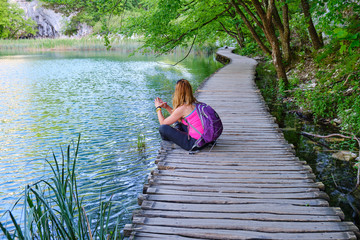 Woman taking a break and meditating on a wooden boardwalk bridge near turquoise waters of Plitvice Lakes, Croatia.
