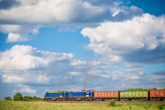 Rural Summer Landscape With Freight Train Hauled By Two Diesel Locomotives Passing Field At Sunny Day 