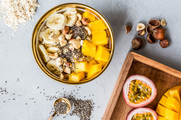 Breakfast oatmeal porridge with fresh fruits, chia seeds and hazelnut on gray background. Oatmeal with mango and banana. Healthy breakfast concept. Flat lay, top view. Mockup, overhead, copy space