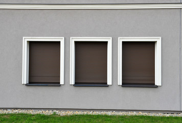 Outdoor three window blinds closed on grey wall.