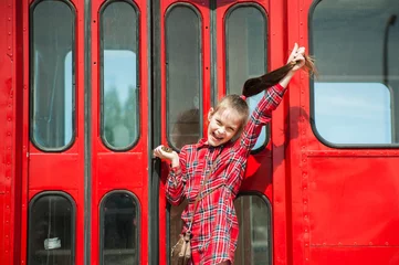 Fotobehang Cute girl with a smile on her face in a red dress near the red bus © Kiryakova Anna