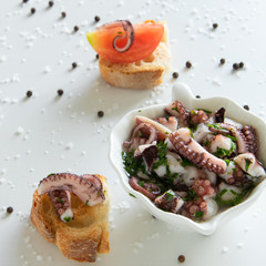 Top view of octopus salad with slices of toasted baguette - bruschetta  on white background with black pepper and sea salt. Typical Mediterranean .appetizer food.