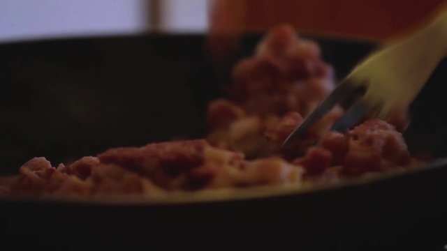 Man is stirring bacon with a fork in a frying pan