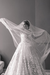 Fototapeta na wymiar Black and white portrait of beautiful bride in wedding dress touchs and throws her veil up in hotel.