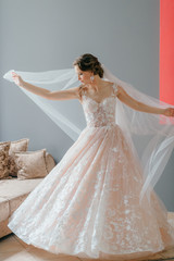 Portrait of beautiful bride in white vintage dress with flower in her hands posing under veil on gray background.