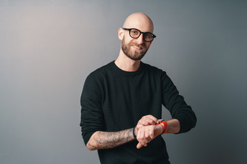 Smiling bearded man wearing a smart watch posing on gray studio background