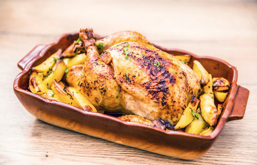 Roasted whole chicken with potatoes in baking dish. Tasty food at home on the kitchen counter