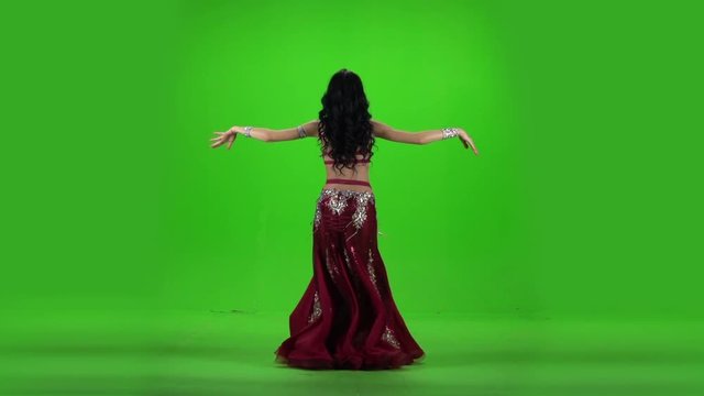 Woman standing back dancing belly dance. Green background. Slow motion