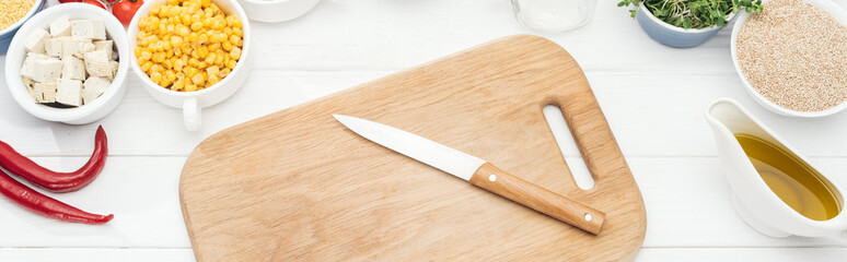 top view of wooden chopping board with knife on white table, panoramic shot
