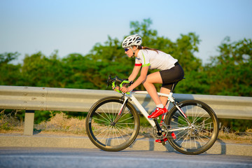 Young Woman Cyclist Riding Road Bicycle on the Highway in the Mountains at Summer. Healthy Lifestyle and Sport Concept.