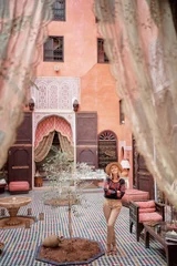 Reisen durch Marokko. Fröhliche junge Frau mit Hut, die sich im traditionellen Riad-Interieur in Medina entspannt. © Loginova