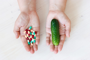 concept in one hand man holding pills in the other cucumber
