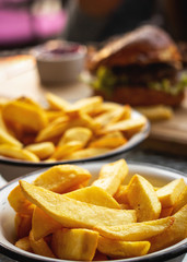 french fries in a plate close-up, on a table in a restaurant, burger in the background