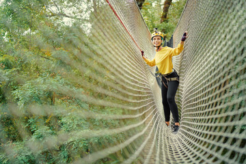Young woman with climbing gear in an adventure extreme park climbing or passing on the rope road.