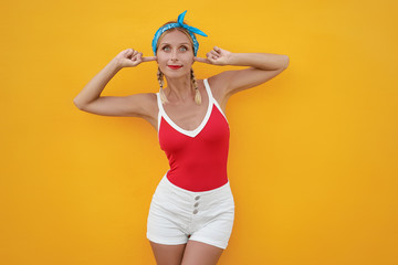 To loud! Young pretty woman closes her ears with fingers refusing to listen to something. Yellow...