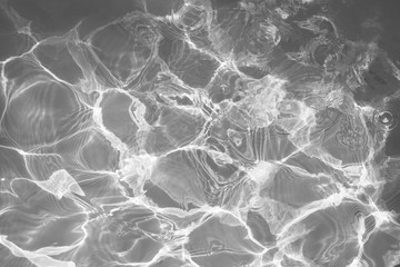 Black and white water surface with bright sun light reflections, water in swimming pool background