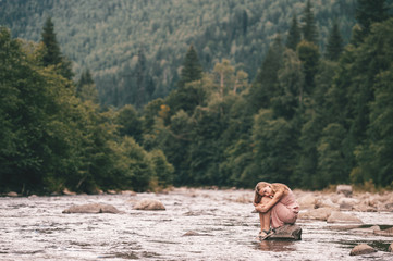 Young lonely girl sitting at stone in the river.