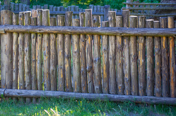 Old wooden fence in garden with plant outdoor on summer day. Old wooden fence made of logs in the form of a palisade