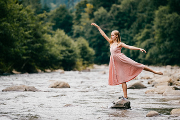 Young graceful ballerina girl balancing on stone in the river. © benevolente