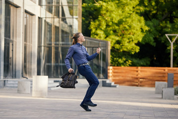 Crazy young businessman dancing on the street with bag. Celebrating victory. Flexibility and grace in business