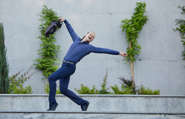 Crazy young businessman dancing on the street with bag. Celebrating victory. Flexibility and grace in business