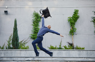 Crazy young businessman dancing on the street with bag. Celebrating victory. Flexibility and grace...