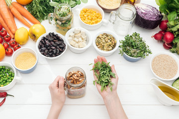 cropped view of woman adding arugula in jar with salad on wooden white table