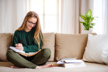 A happy young female student sitting on sofa, studying.