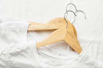 White pure cotton T-shirts on wooden hangers laying on linen cloth. Casual unisex clothes natural materials shopping sale concept. Poster banner with copy space