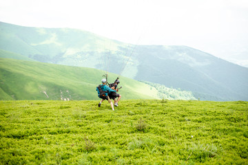 Men starting a paraglider flight, running on the green meadow high in the mountains