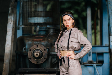 Beautiful young stylish girl posing at abandoned factory outdoor with an old broken engine.