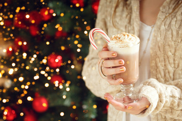 Girl holding cacao with whipped cream and peppermint candy cane. Christmas holiday concept. Horizontal. Festive holiday celebration bokeh