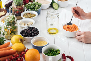 cropped view of woman adding couscous in glass jar on wooden white table