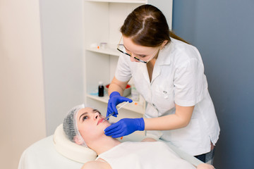 The doctor cosmetologist makes Lip augmentation procedure of a beautiful woman in a beauty salon. Cosmetology skin care.