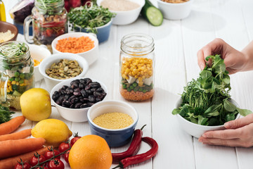 cropped view of woman taking greenery from bowl on wooden white table