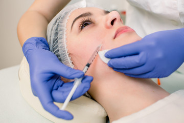 The doctor cosmetologist makes the Botulinotoxin injection procedure for tightening and smoothing wrinkles on the face skin of a beautiful, young woman in a beauty salon.Cosmetology skin care.