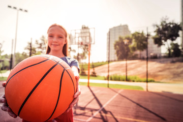 Smiling good-looking girl tightly holding bright basketball ball