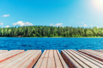 Wooden timber of a rural mooring on a lake in the middle of the forest. A peaceful river dock in the woods.Sunny footbridge. Minimal background with blue sky,clean lake and mooring in the country side - Powered by Adobe
