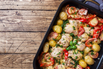 Baked chicken thighs, potatoes and vegetables in a baking tray on a wooden table. Copy space.