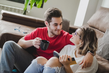 A couple reads a book and drinks coffee on the couch at home