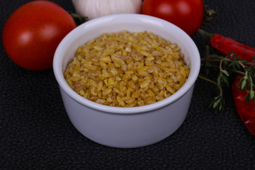 Raw bulgur in the bowl with tomatoes and garlic