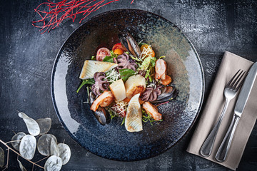 Top view on seafood salad with squid, shrimp, scallops, mussels, baby octopus, cherry tomato and greens. Salad bowl served on restaurant table. Top view food. Copy space