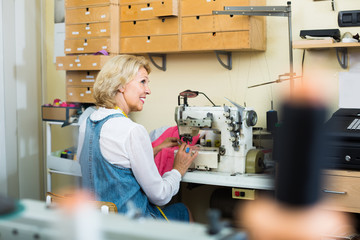 attentive middle-aged woman tailor using sewing machine