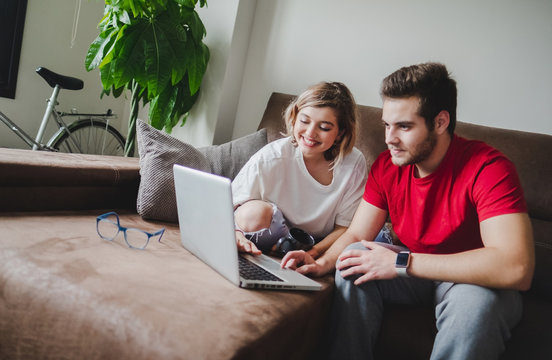 A young couple rests on the couch at home while using the laptop