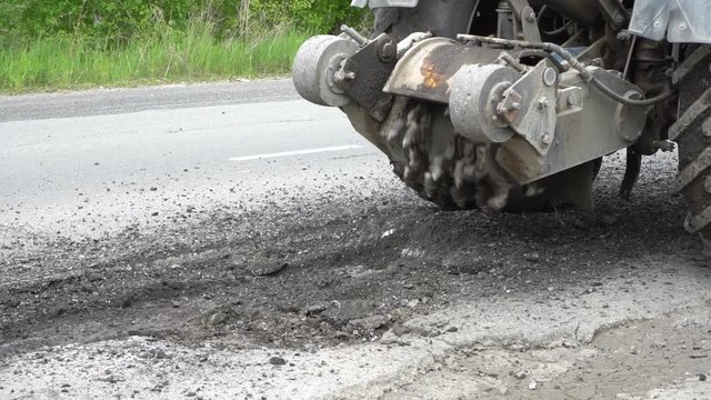 Road milling machine cuts the old asphalt. Road repair. Destruction of the road surface. The cutter cuts a layer of asphalt. Pieces of stone fly apart. Close-up