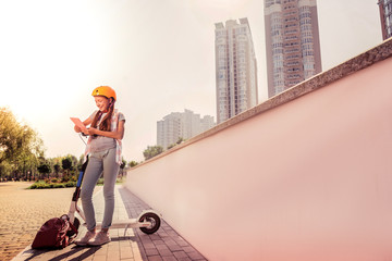 Cheerful skinny girl in light jeans leaning on a calm scooter