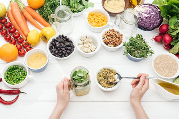 cropped view of woman adding pumpkin seeds in jar with salad on wooden white table