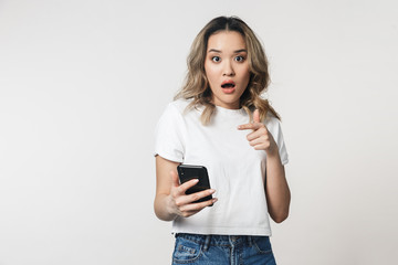 Shocked emotional cute young woman posing isolated over white wall background using mobile phone.