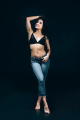 Fototapeta premium sexy happy brunette barefoot woman in blue jeans and bra posing isolated on black