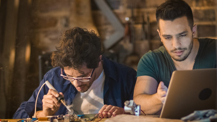 Two students are studying electronics and soldering in a garage.